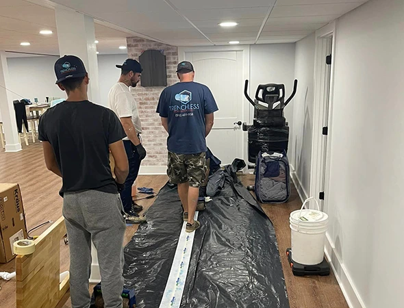 Three men are installing piping on a basement floor, showcasing their expertise in professional pipelining services.