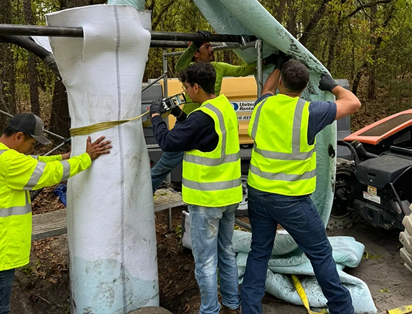 Workers are installing a large white pole as part of a trenchless plumbing project, ensuring minimal disruption to the area.