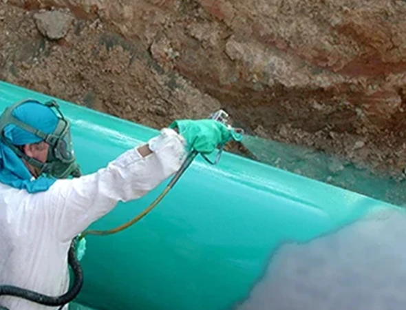 A man in a white coat applies green paint to a pipe, indicating ongoing sewer repairs in a maintenance setting.