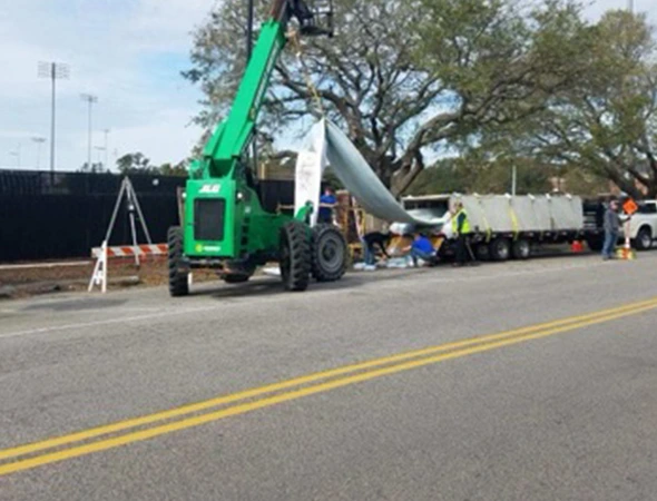 A crane is hoisting a large piece of equipment onto a truck, facilitating essential sewer repairs in the area.