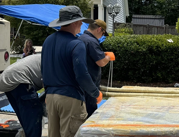 A team of men in blue shirts and orange gloves works together on a large sheet of plastic, showcasing trenchless plumbing methods.