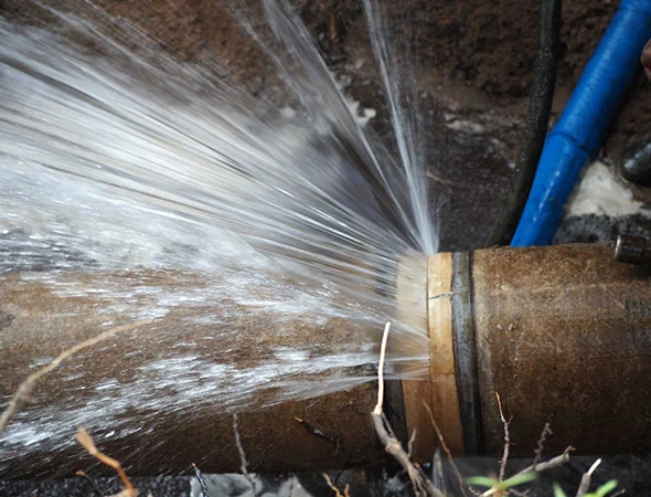A burst pipe sprays water forcefully, creating a high-pressure stream. The image highlights the urgency and chaos of the leakage situation.