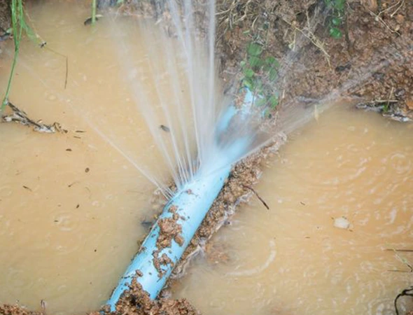 A burst pipe releases water into the ground, showcasing a key aspect of trenchless pipe restoration practices.