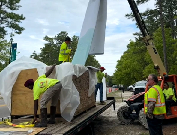 Workers are loading a large wooden piece onto a truck, showcasing the logistics involved in trenchless plumbing projects.