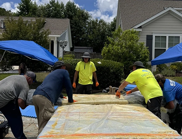 A team of men focused on a large mattress, demonstrating their collaborative efforts related to trenchless plumbing work.