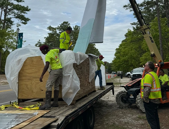 Workers are loading a large wooden piece onto a truck, showcasing the logistics involved in trenchless plumbing projects.